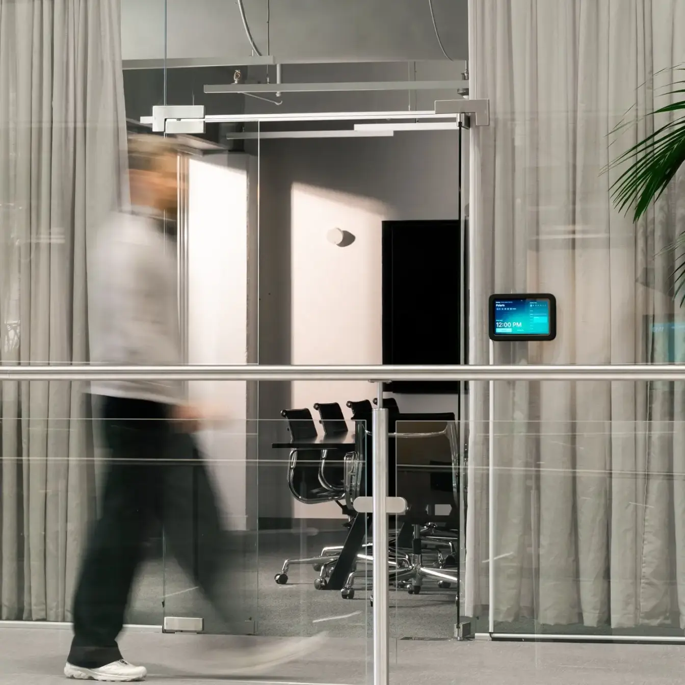 A blurred person walks past a glass-walled conference room with chairs visible inside.
