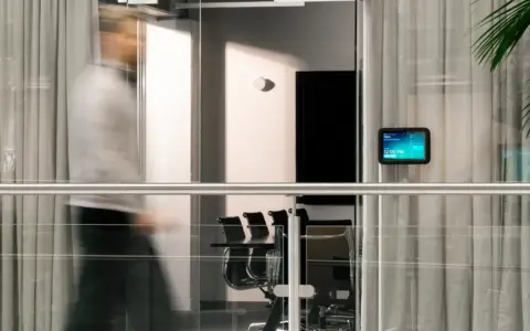 A blurred person walks past a glass-walled conference room with chairs visible inside.