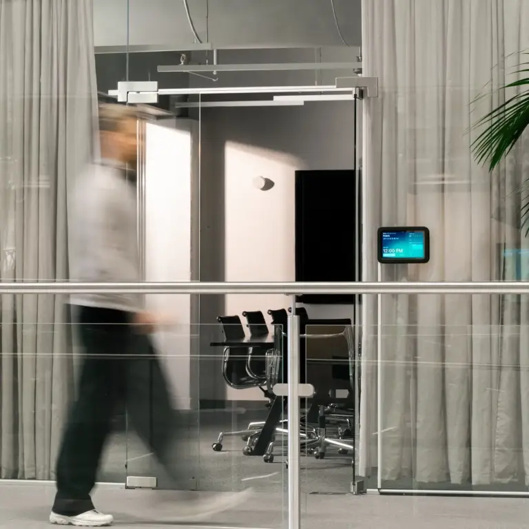 A blurred person walks past a glass-walled conference room with chairs visible inside.