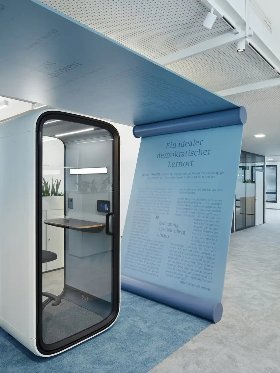 Modern office interior featuring a white Framery One Compact pod with a glass door.