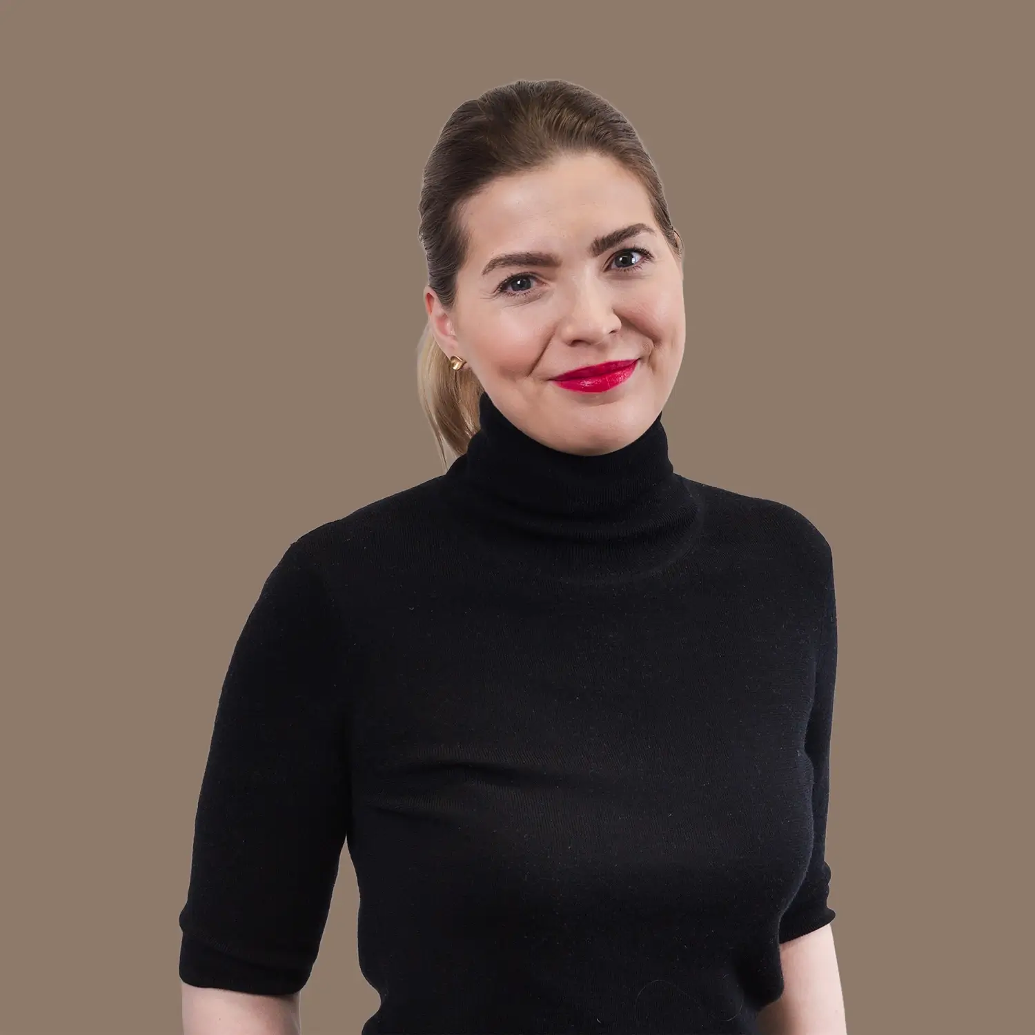 A woman with her hair tied back wearing a black turtleneck smiles at the camera against a plain brown background.