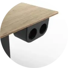 Close-up of a wooden desk edge with a black rectangular cable management block featuring two circular holes.