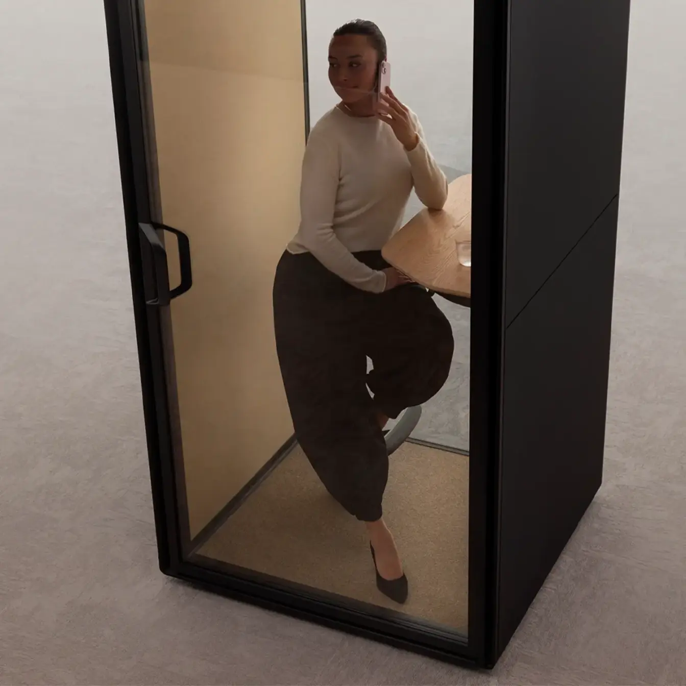 Woman posing inside a Framery Gradus Focus pod, wearing a light sweater and dark pants, with one leg bent and looking at the camera.