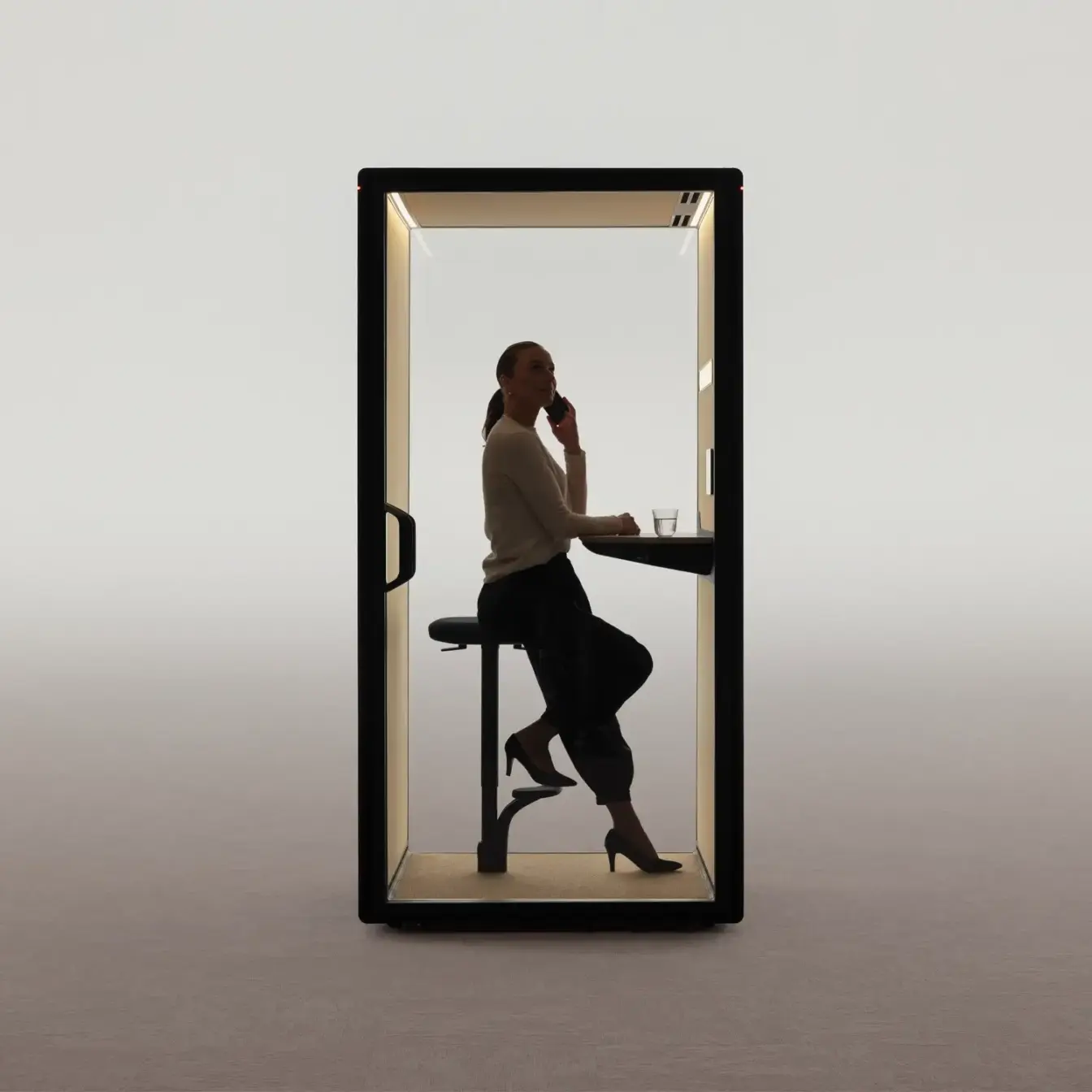 Silhouette of a person sitting on a stool inside a glass walled Framery Gradus Focus pod against a white background.