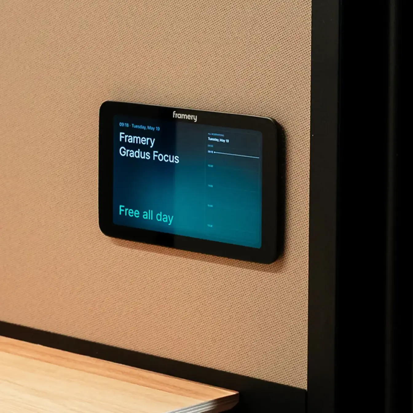 A Framery Gradus Focus touchscreen panel on a beige interior wall.