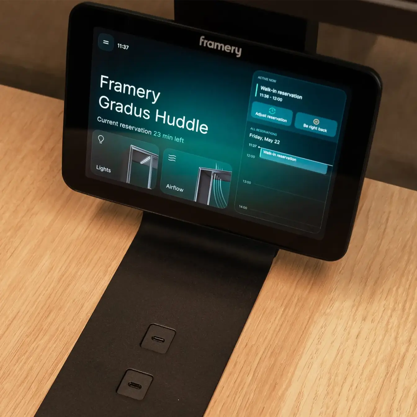 Framery Gradus Huddle touchscreen interface on a black stand placed on a wooden desk.