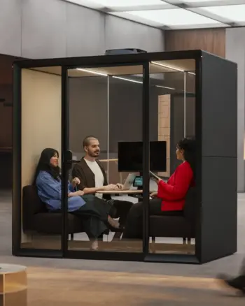 Three colleagues sit around a table inside a Framery Gradus Huddle smart and soundproof huddle room in a modern office.