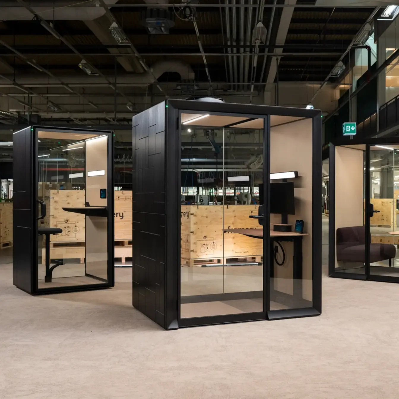 Three glass-walled Framery Gradus smart and soundproof pods with black frames sit in an open industrial interior.