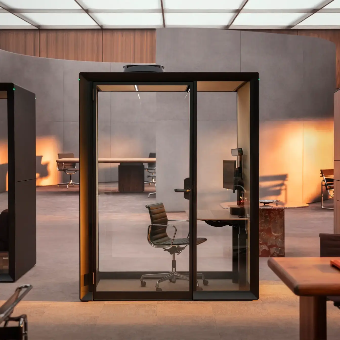 A glass-enclosed Framery Gradus Work pod with a desk and chair inside a modern coworking space.