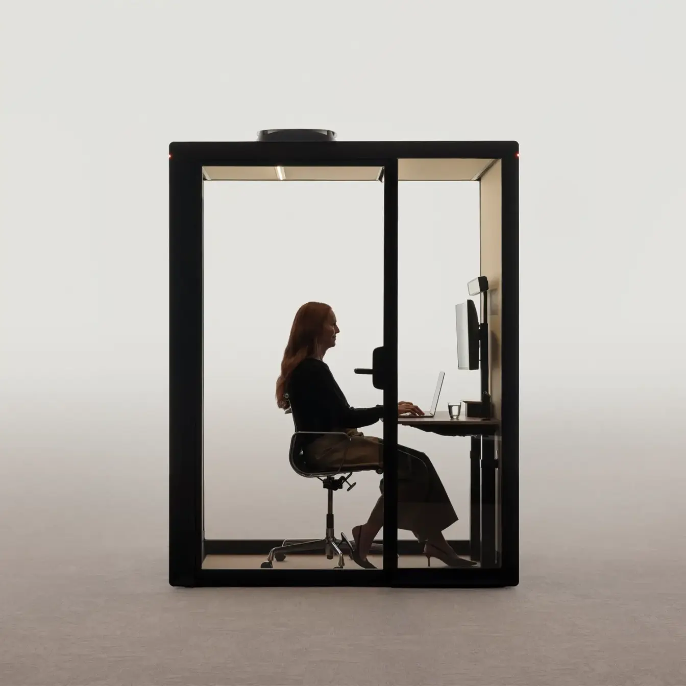 A person sits at a desk inside a glass-walled Framery Gradus Work smart and soundproof work pod.