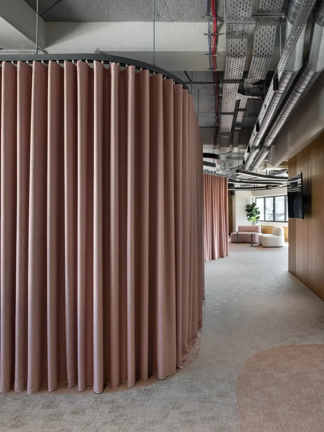 Interior space featuring a curved pink curtain partition with exposed ceiling ducts and a seating area visible in the distance.