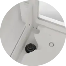 Close-up of a white corner showing a circular drain and a black object nearby.
