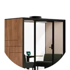 A modern glass-walled office pod featuring a wooden cabinet on the left and a small desk with a chair inside.
