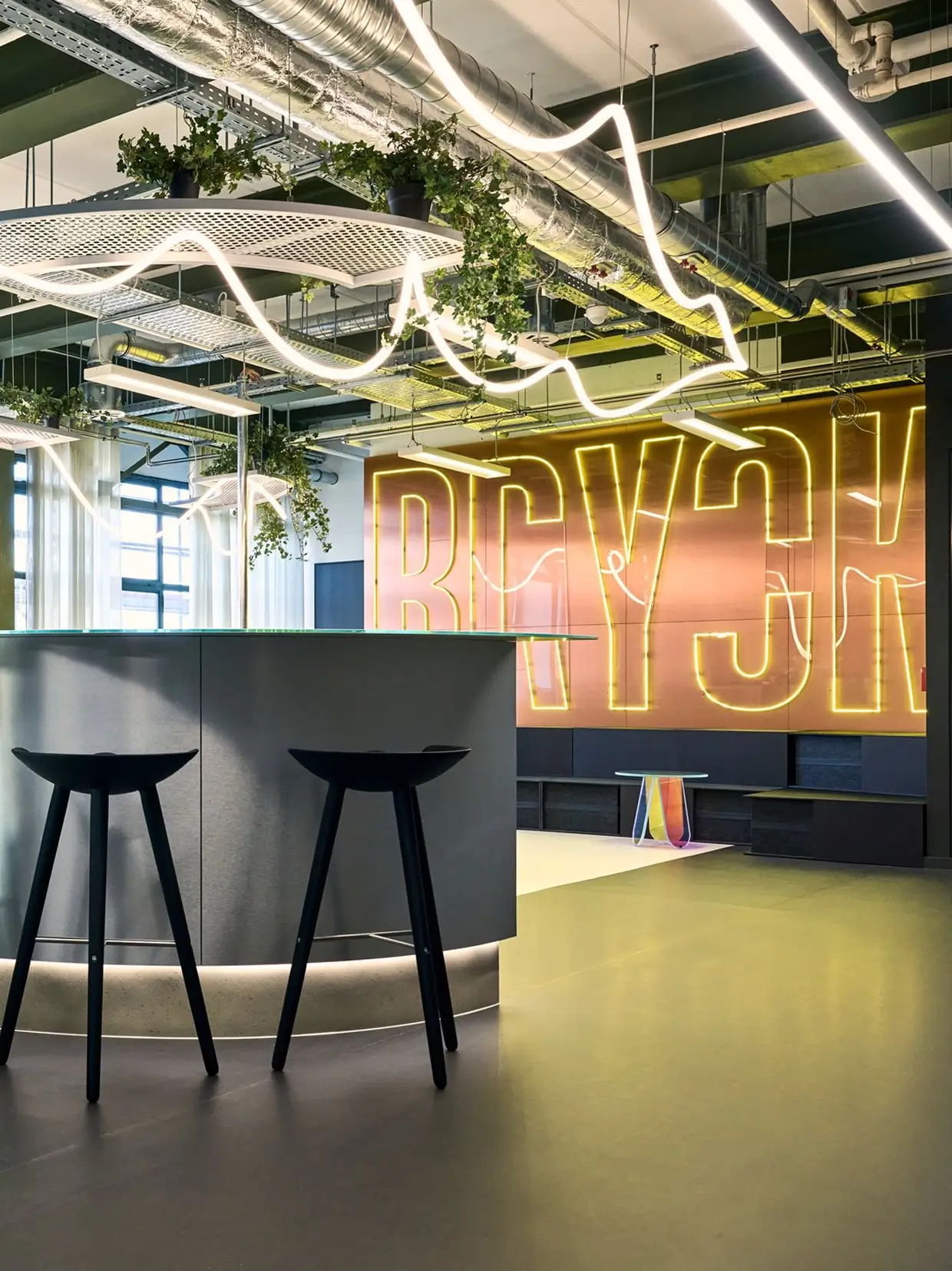 A table with bar stools with snakelike led lights hanging from ceiling and a neon sign at the back wall.