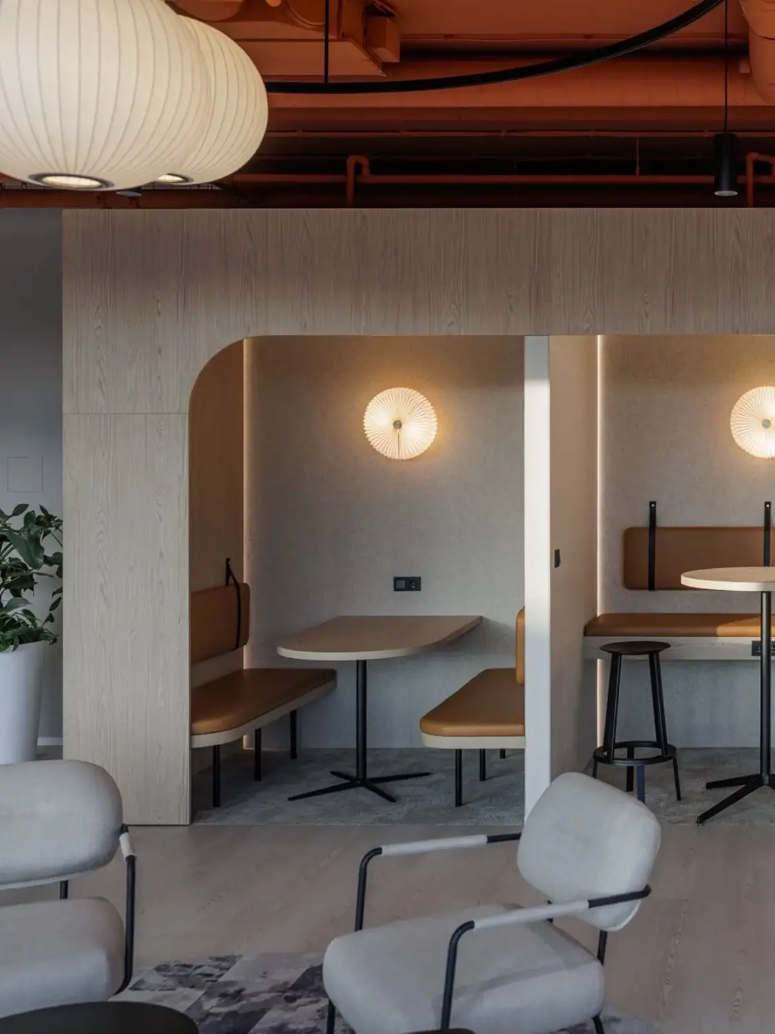 A modern cafe interior with semi-private booth seating, round tables, and warm ambient lighting.
