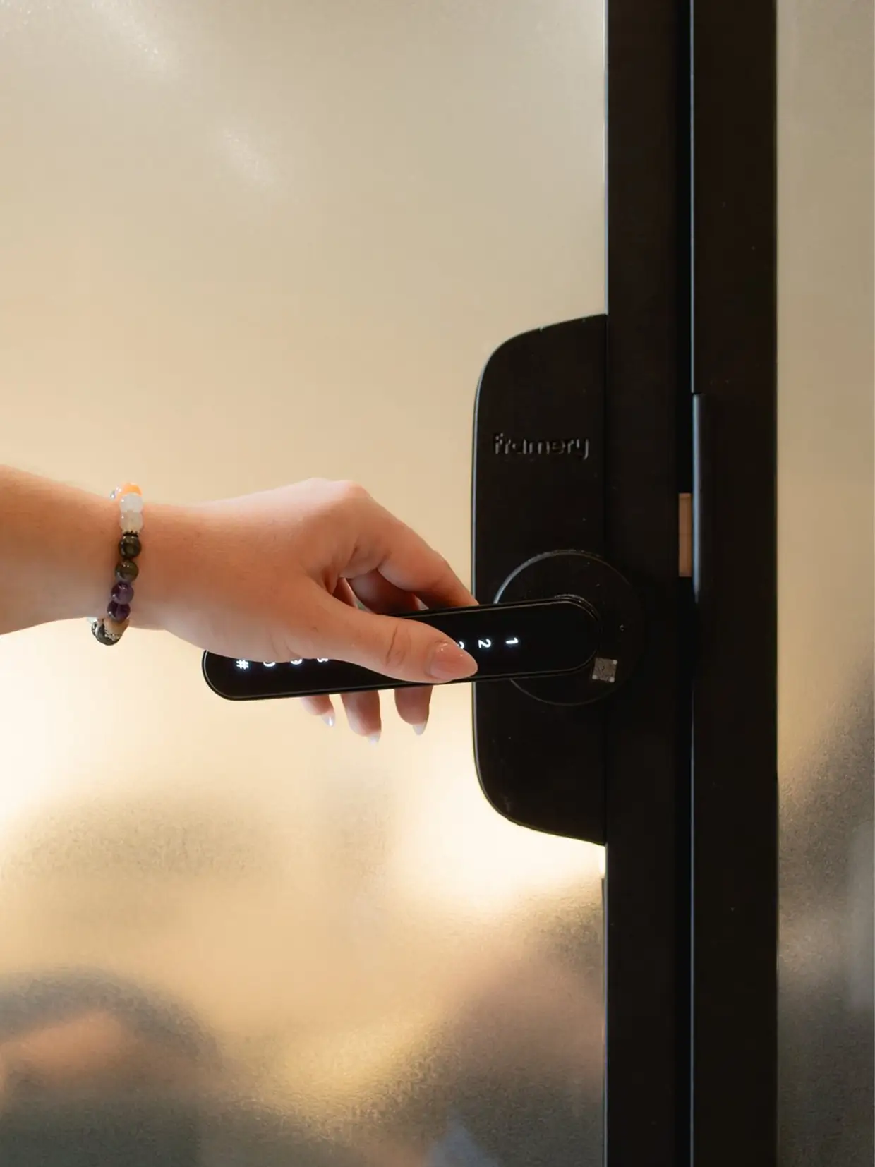 A hand with a bracelet grabbing a black door handle with a smart lock.