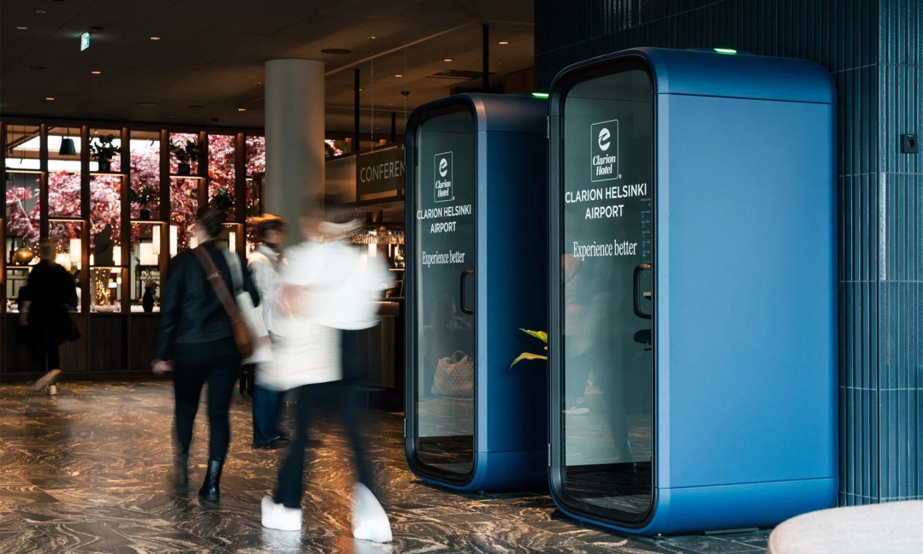 Blue Framery One Compact phone booths lined up in a modern indoor corridor with blurred people walking by.