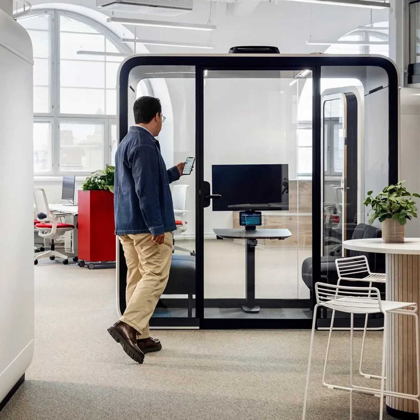 A man walks past a glass-walled meeting pod in a modern office.