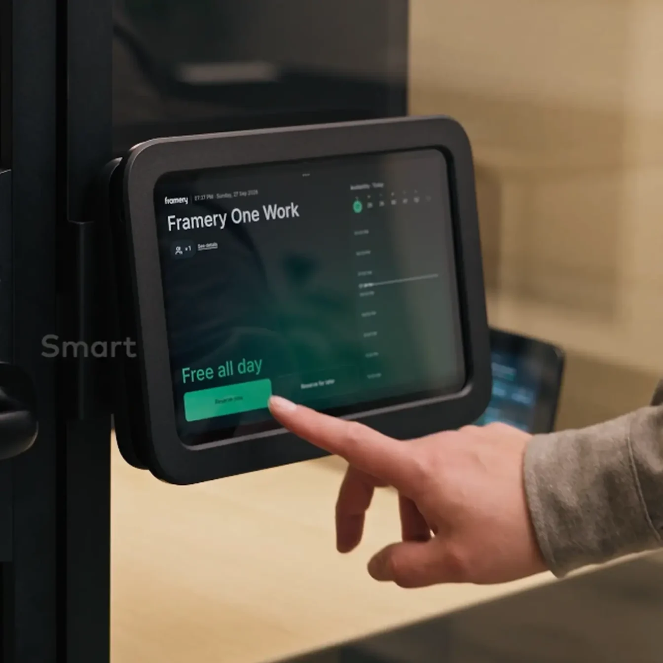 A hand taps a wall-mounted touchscreen panel labeled Framery One Work, displaying a green “Free all day” button.