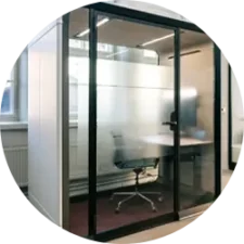 A glass-walled office pod with a desk, chair, and computer inside.