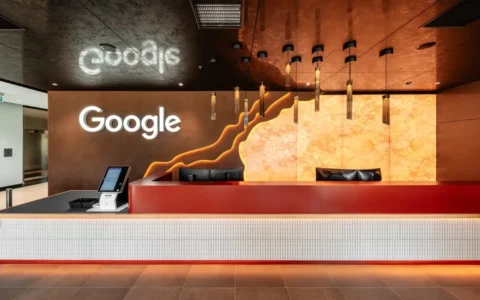 Modern Google office reception with a white counter, warm orange wall art, and the Google logo.