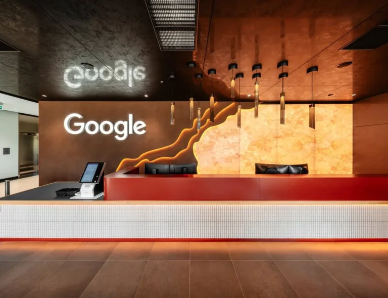 Modern Google office reception with a white counter, warm orange wall art, and the Google logo.