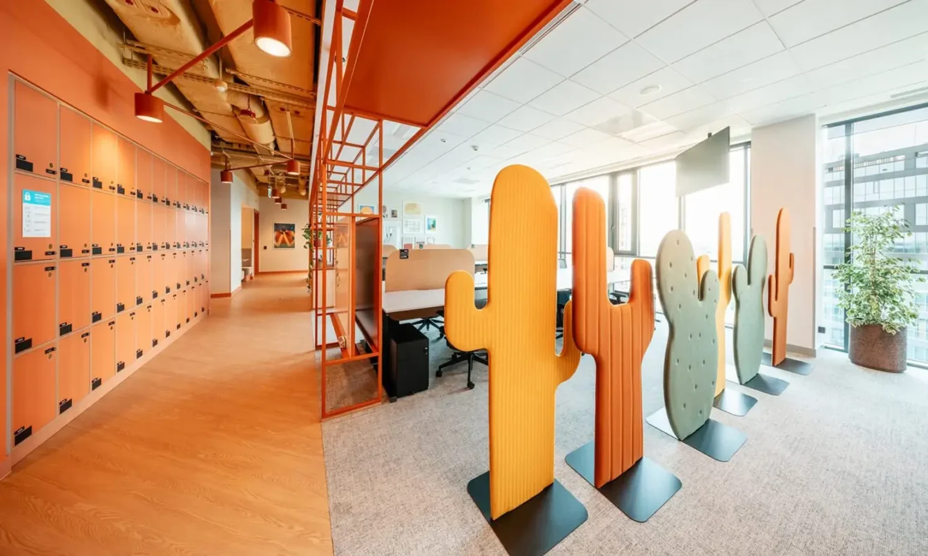 Bright modern office space with orange lockers along the left wall and colorful cactus-shaped partitions on the right.