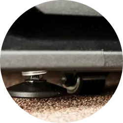 Close-up of a small caster wheel attached to the bottom of a piece of furniture resting on a beige carpet.